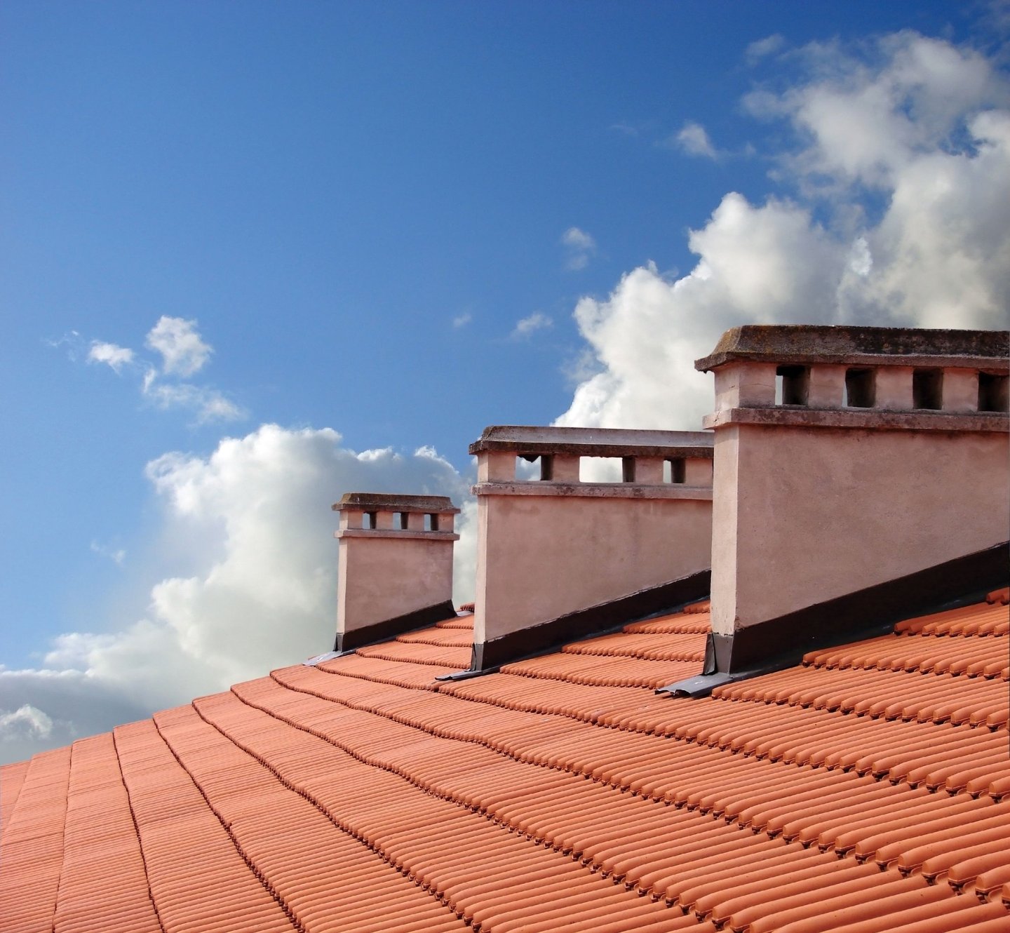 clay roof shingles with 3 white chimneys with a  blue sky background and clouds