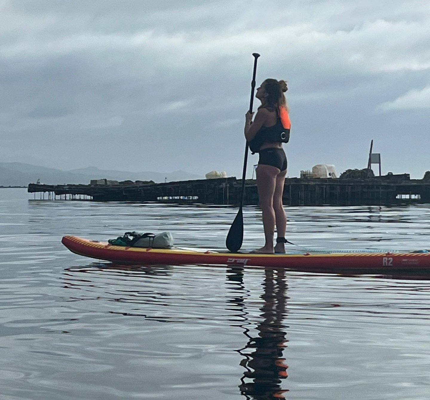 Chica sobre una tabla de paddel surf junto a una batea mientras hace el camino de santiago