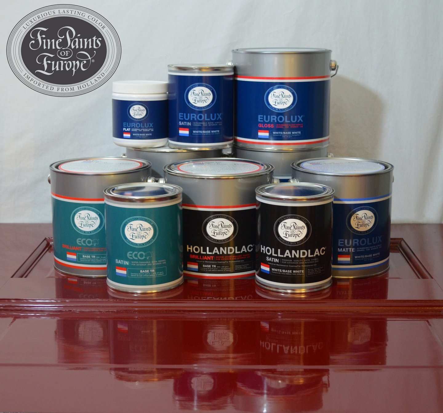 Assorted cans of Fine Paints of Europe Hollandlac and Eurolux paints displayed on a high-gloss red surface.