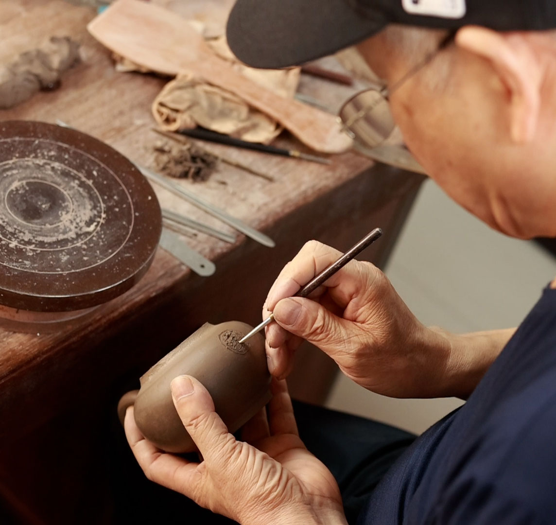 hand holding a tool, making a hole in the body of a teapot
