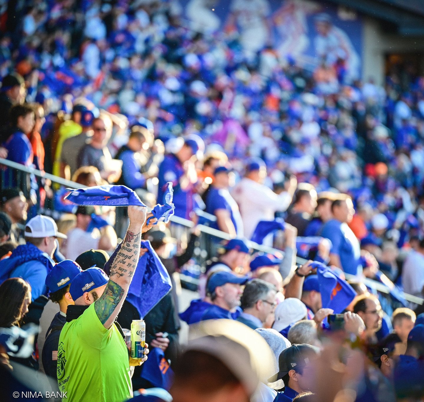 excited mets fans wearing blue and orange baseball caps waving rally towels at the nlcs