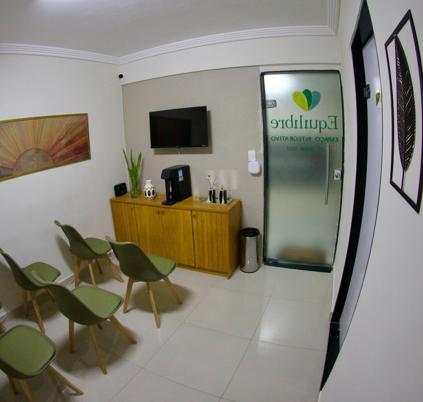 Modern clinic waiting room with green chairs, wooden cabinet, and wall art in a wellness center.
