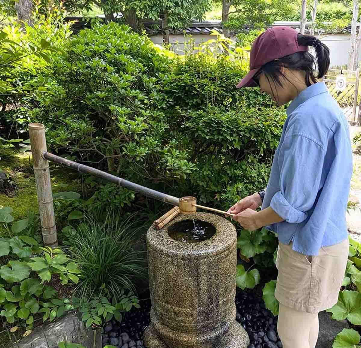 Woman using a traditional stone water basin in a Japanese garden.