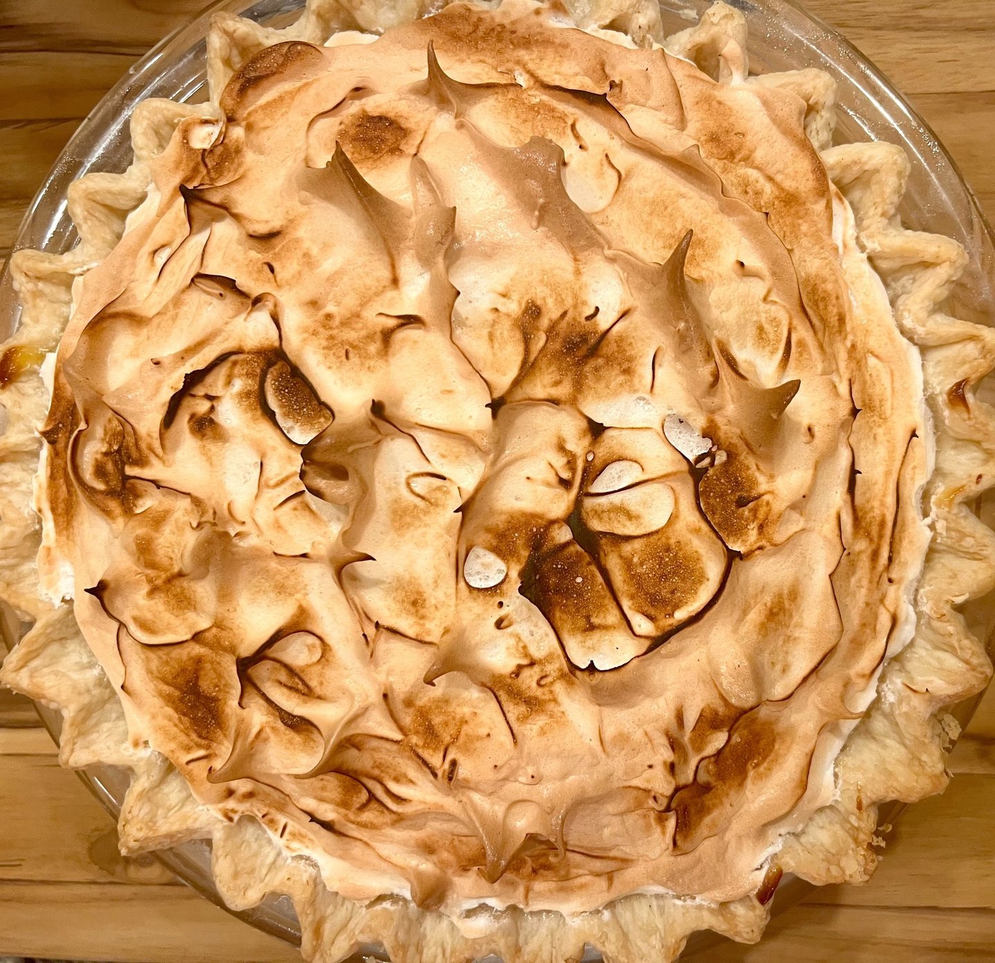 A homemade lemon meringue pie with a toasted golden brown marshmallow topping in a glass baking dish.