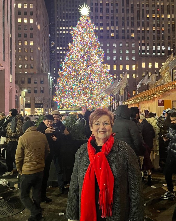 Photo of Debbie in front of a giant, multicolored Christmas tree in a crowded urban plaza.