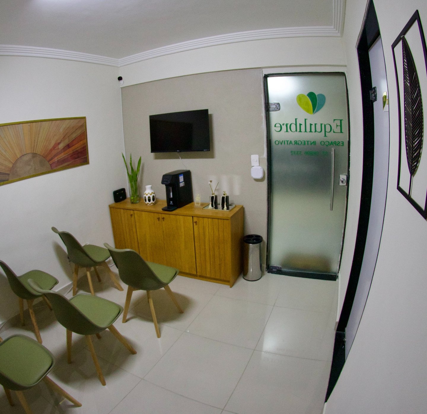 Modern clinic waiting room with green chairs, wooden cabinet, and wall art in a wellness center.