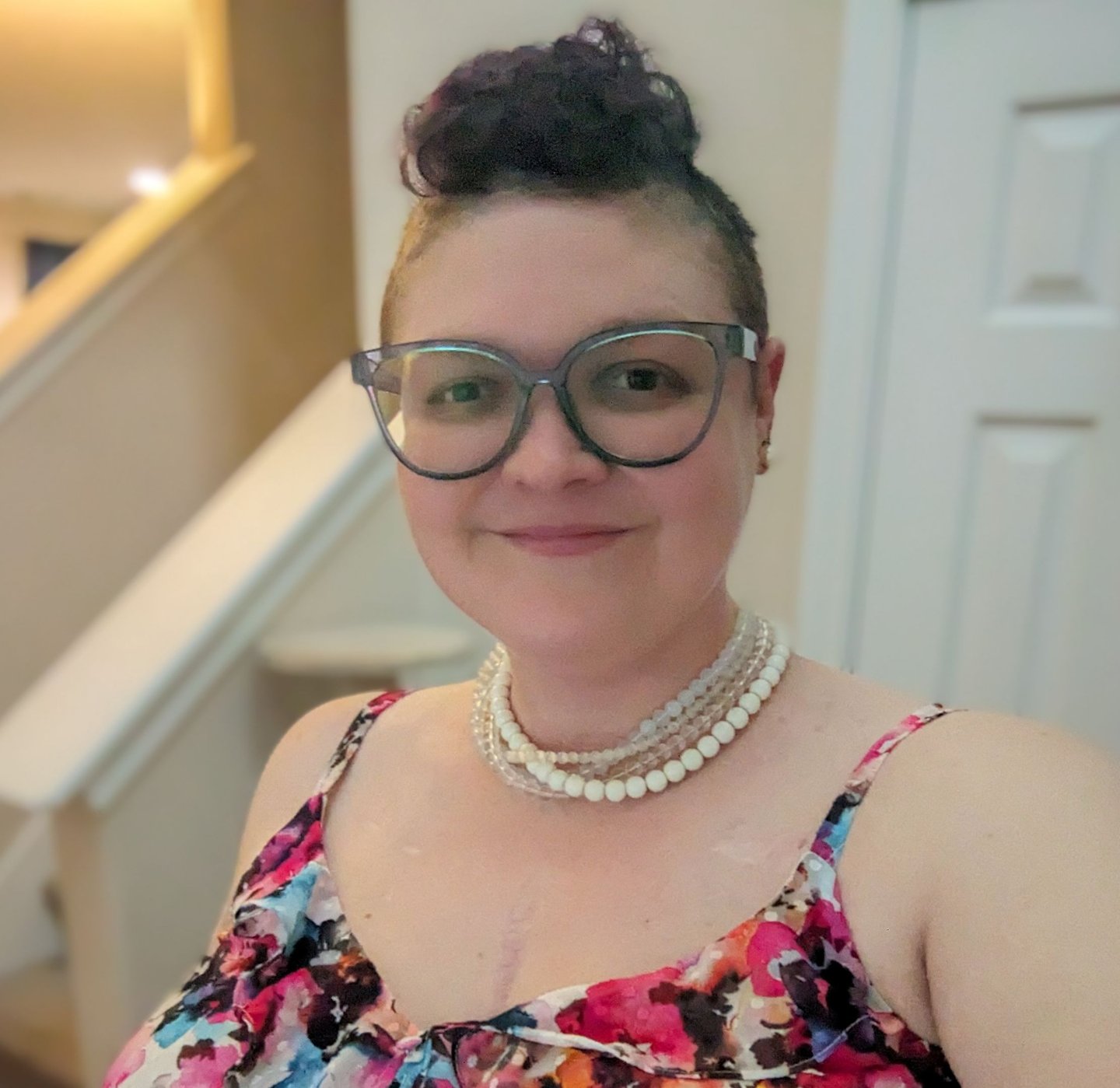 Picture of Megan, a smiling woman with a blue mohawk and pearls.