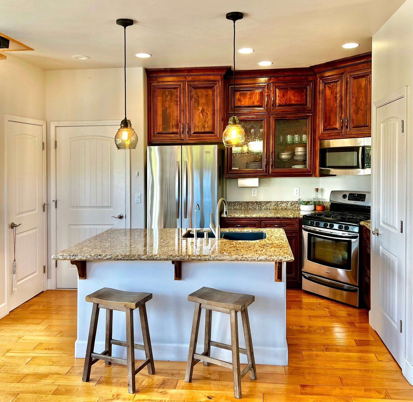 A kitchen with a warm wood cabinet stain, glowing granite countertops, and hand scraped wood floors.