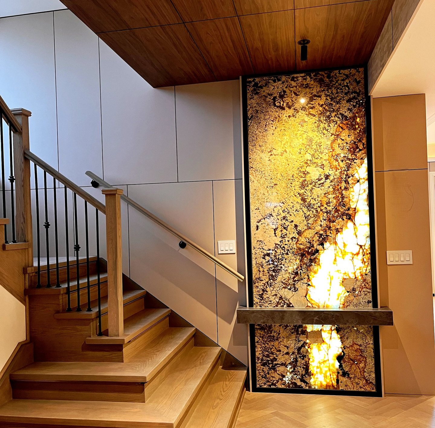 Modern wood staircase featuring a backlit onyx stone wall panel and elegant hardwood flooring.