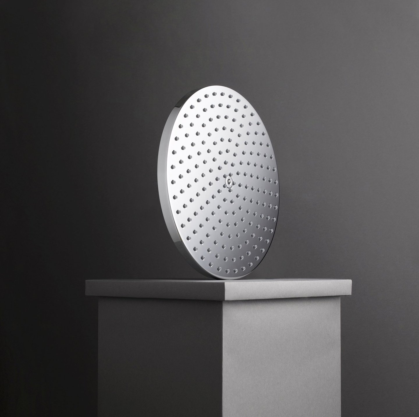 chrome rain shower head balanced on grey plinth