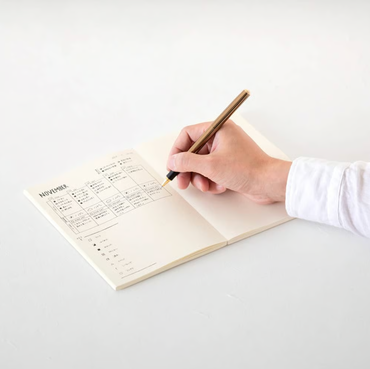 A hand writing with a gold fountain pen in a minimalist November monthly planner notebook.