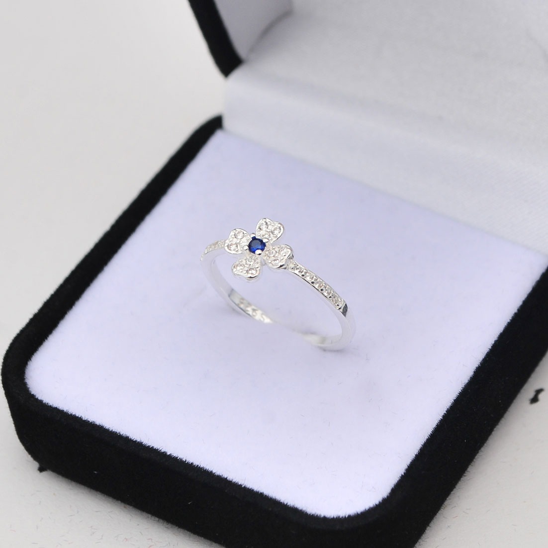 Sterling silver four-leaf clover ring with blue sapphire center in a black velvet jewelry box.