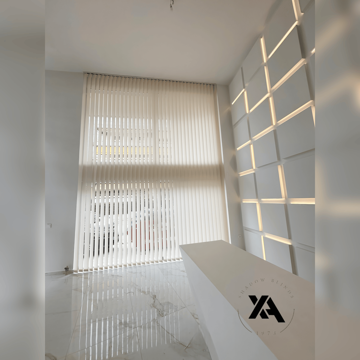 Modern office reception area with white vertical blinds covering large windows and a contemporary white reception desk.
