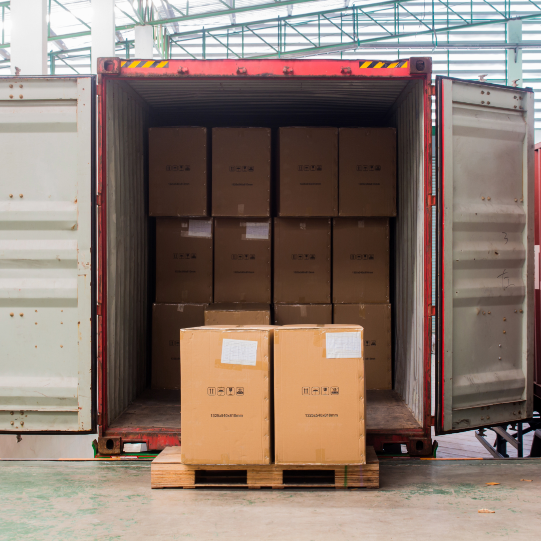 Stacked cardboard boxes inside an open red shipping container for freight transport.
