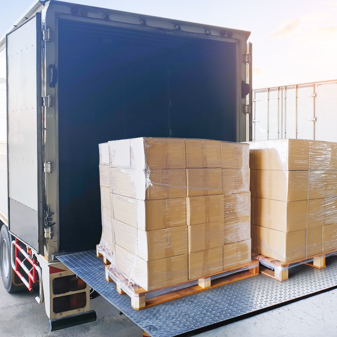 Stacked cardboard boxes on pallets being loaded into a delivery truck for shipping logistics.