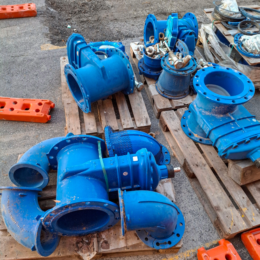 Industrial blue ductile iron flanged pipe fittings and valves on wooden pallets at a construction site.