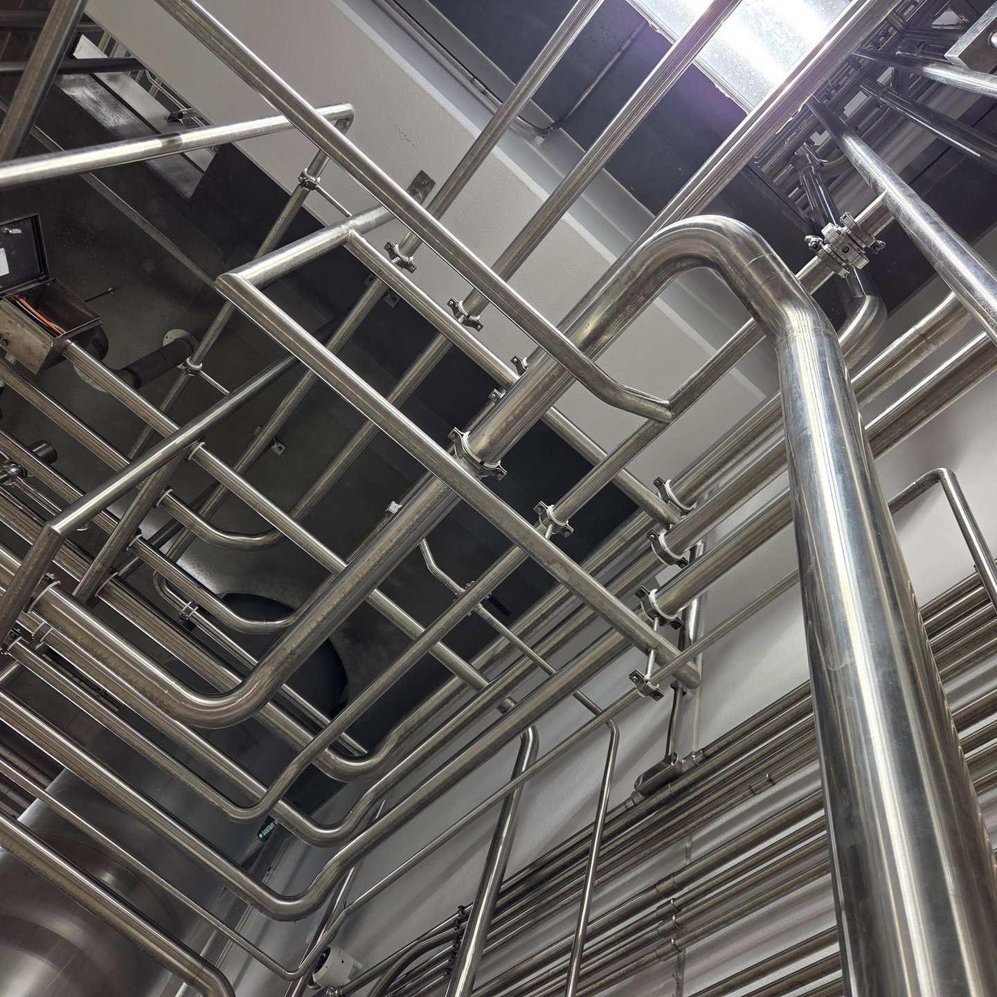 Wide view of industrial stainless steel piping and plumbing fixtures in a modern factory facility.