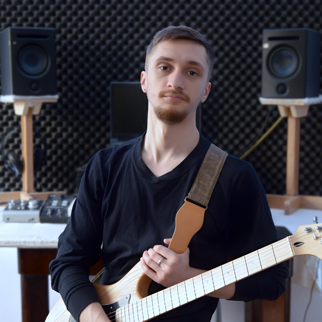 Music artist Valah looking at the camera in a studio, with electric guitar strapped on his shoulder.