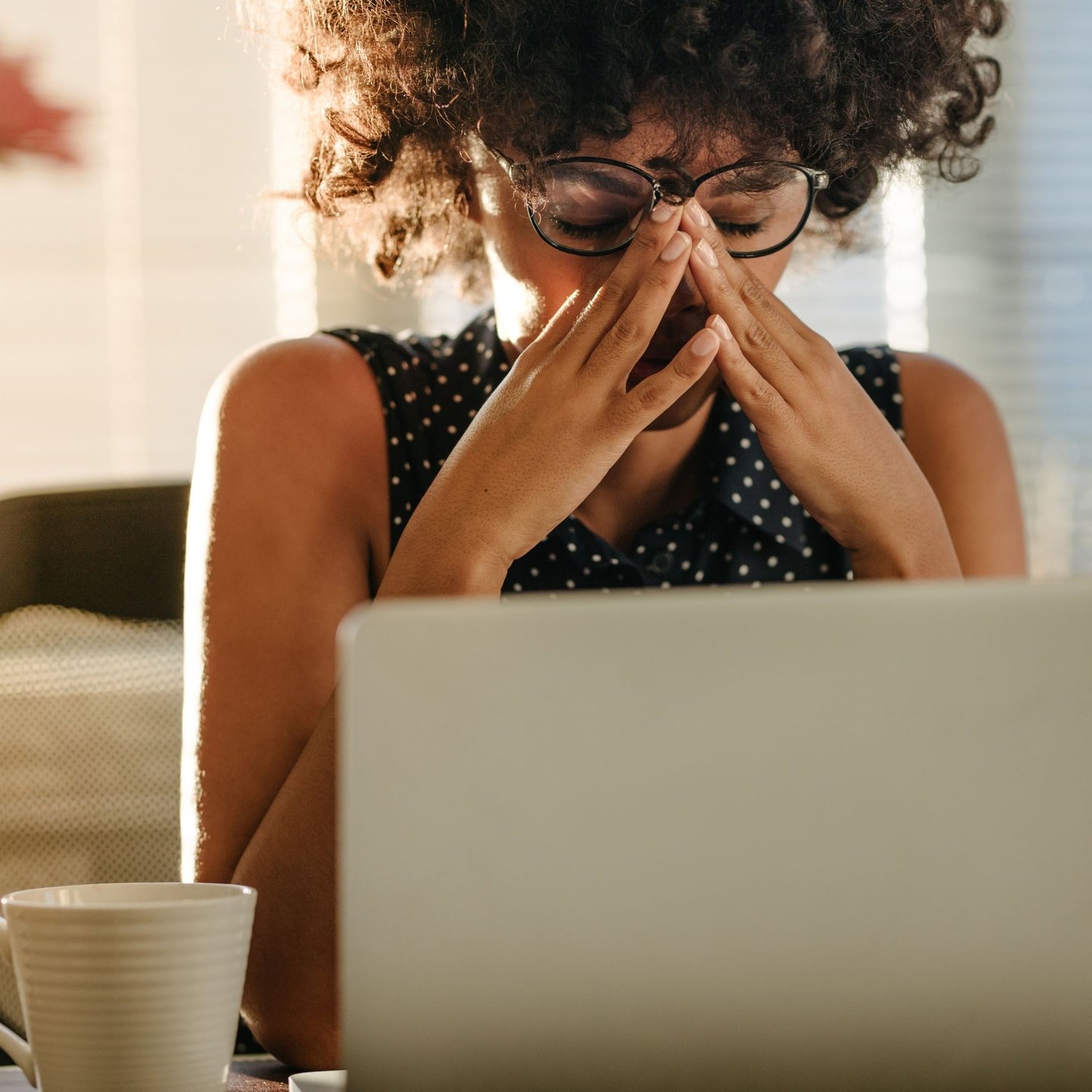 A person looking stressed and overwhelmed while working at a laptop with multiple open tabs and a coffee cup