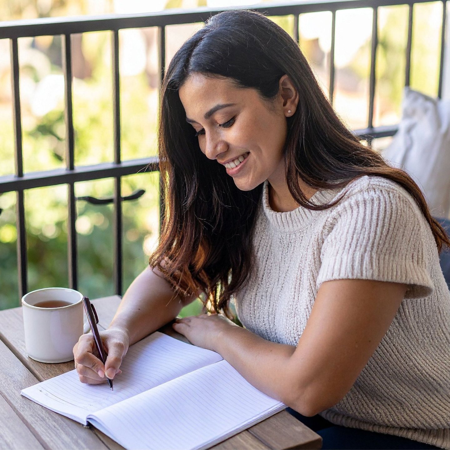 A woman in Calgary journaling on a couch in soft natural window light, notebook open, cup of tea beside her