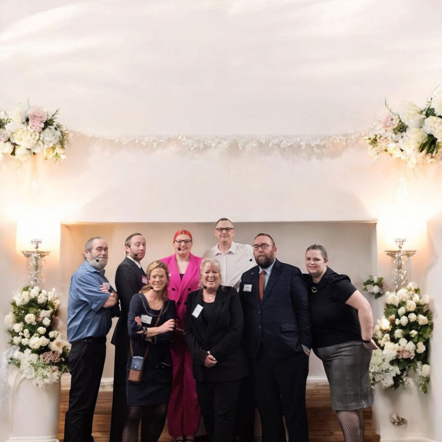 A group of professionals posing together at a business event with floral decorations and warm lighting.