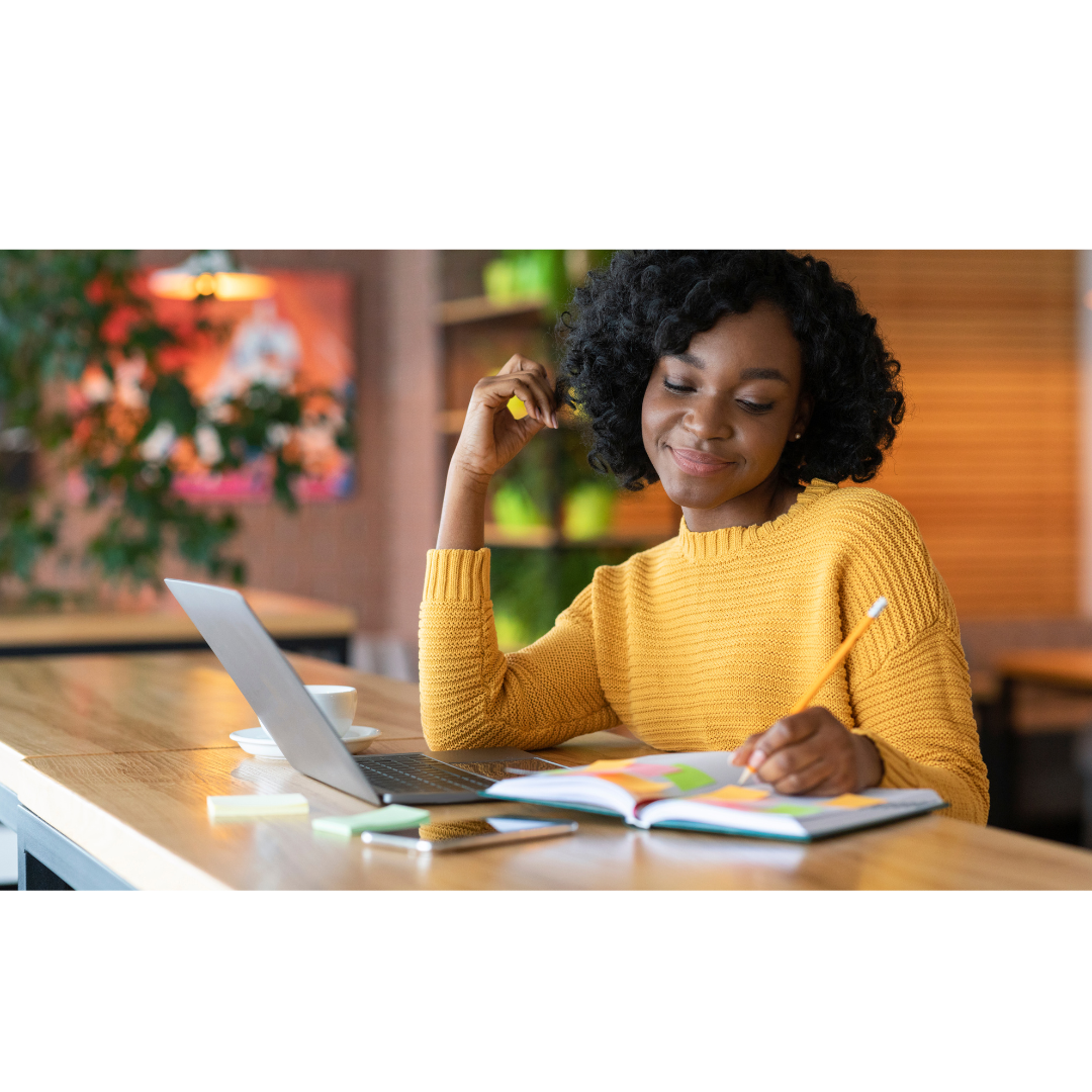 Femme souriante en pull jaune, écrivant dans un carnet avec un ordinateur