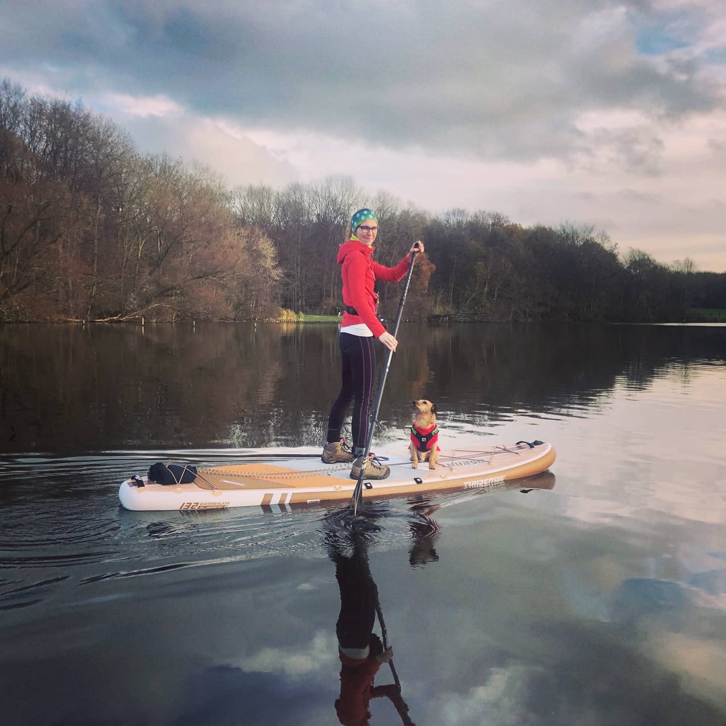 Rita Dekšnytė paddleboarding on a calm lake with her dog