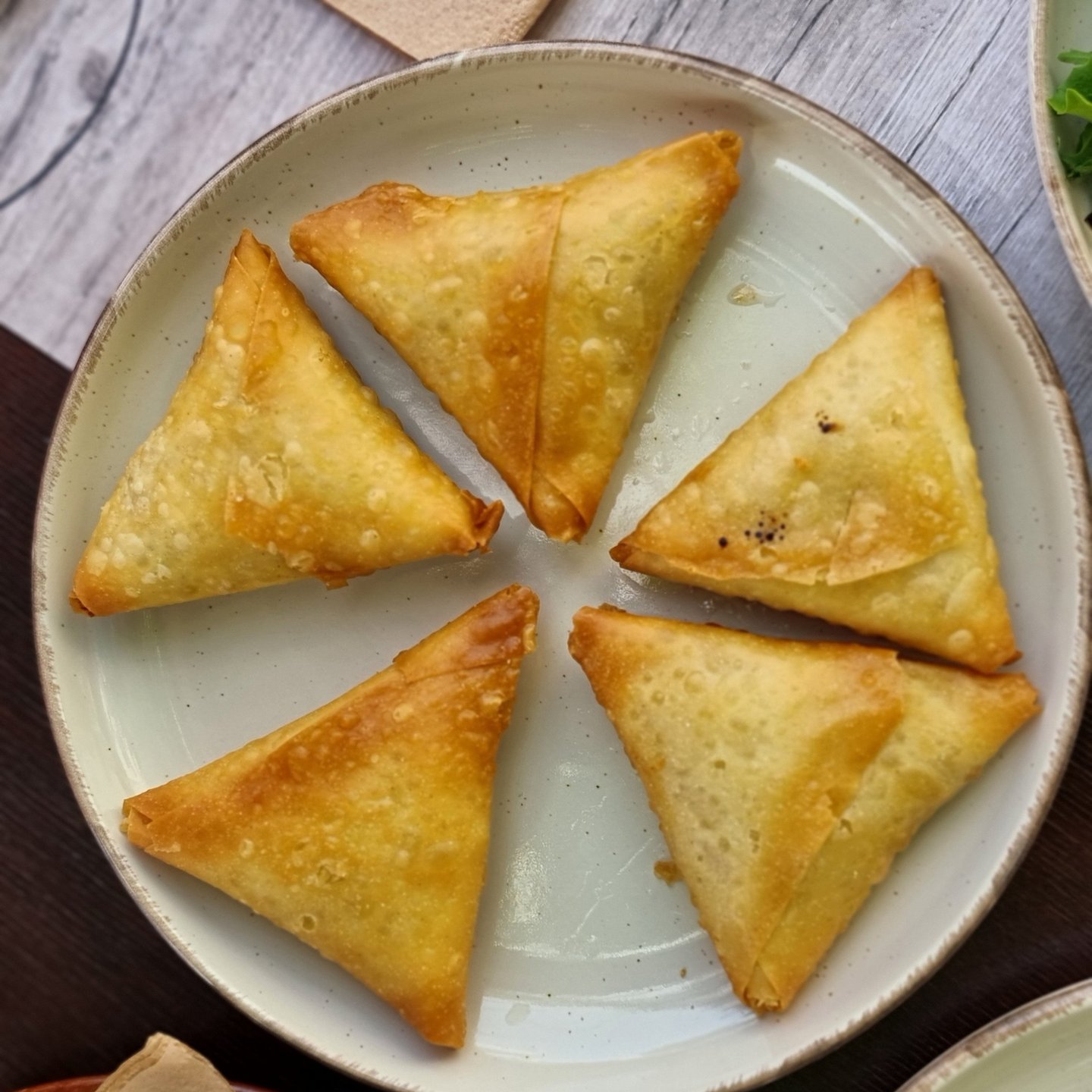 A plate of five golden-brown, crispy triangular vegetable samosas arranged in a circle.
