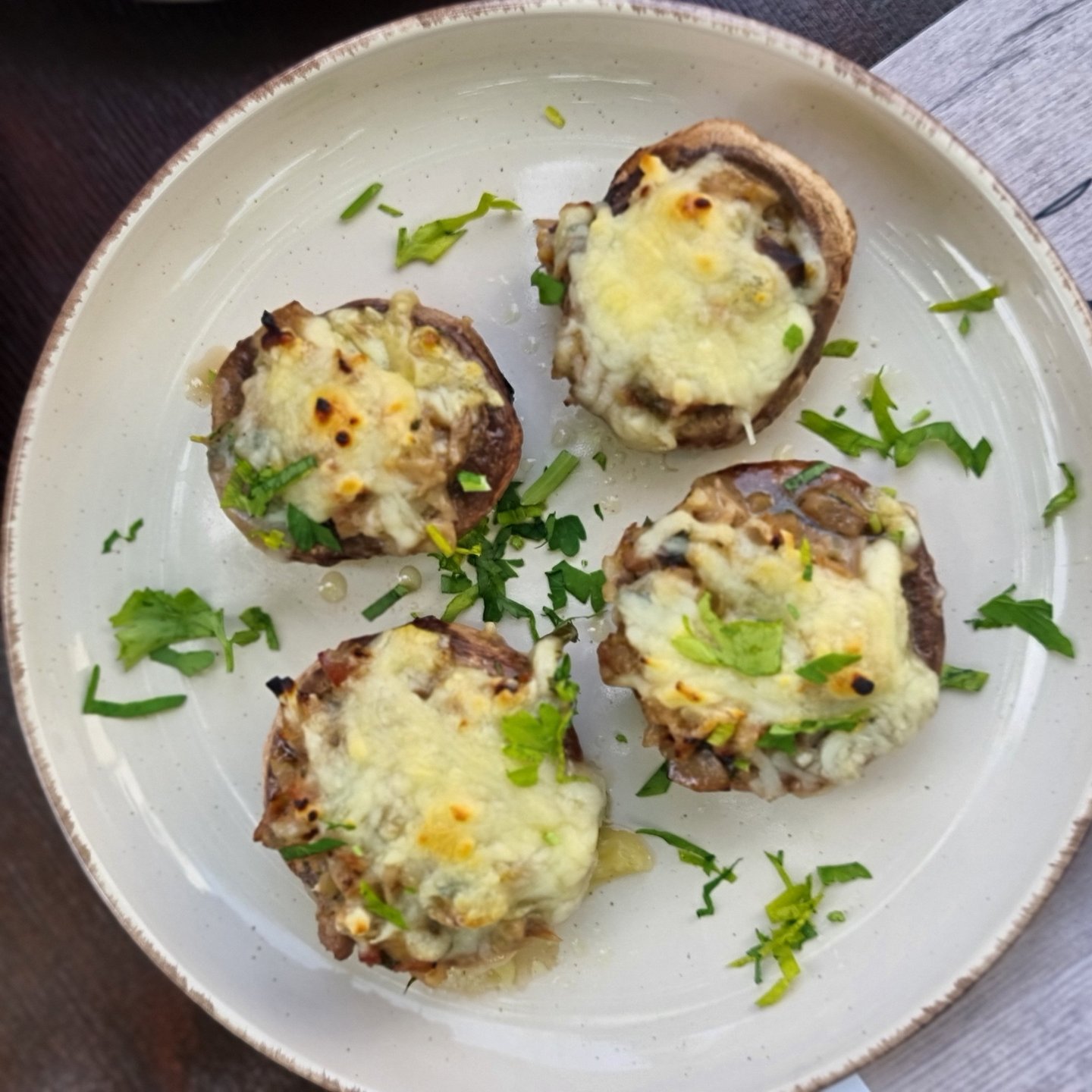 Four cheesy stuffed mushrooms garnished with fresh herbs on a white ceramic plate.