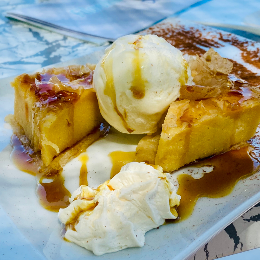 Warm Greek orange cake served with vanilla ice cream and honey syrup on a white plate.
