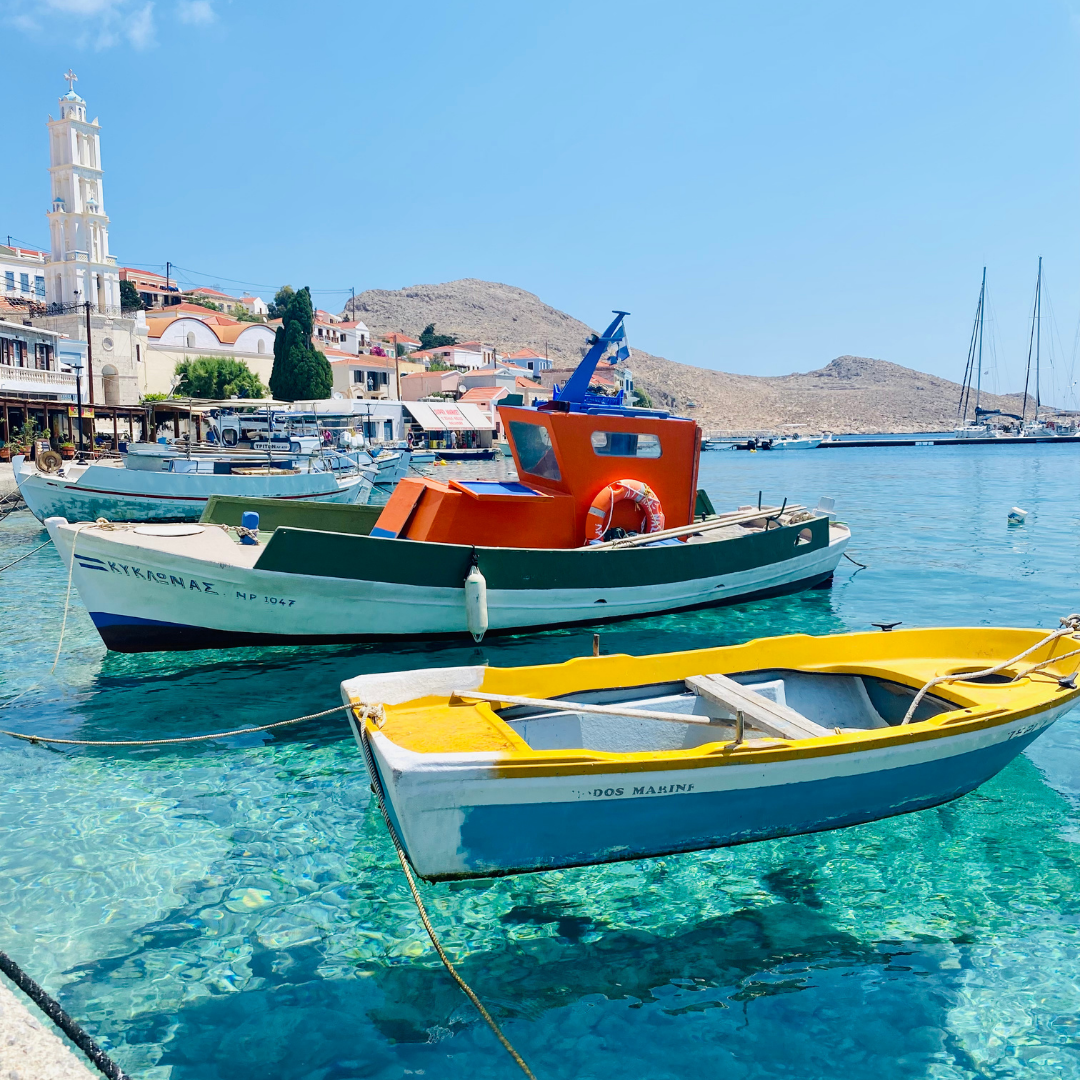 Traditional fishing boats floating on clear turquoise water at the scenic harbor of Halki Island in Greece.