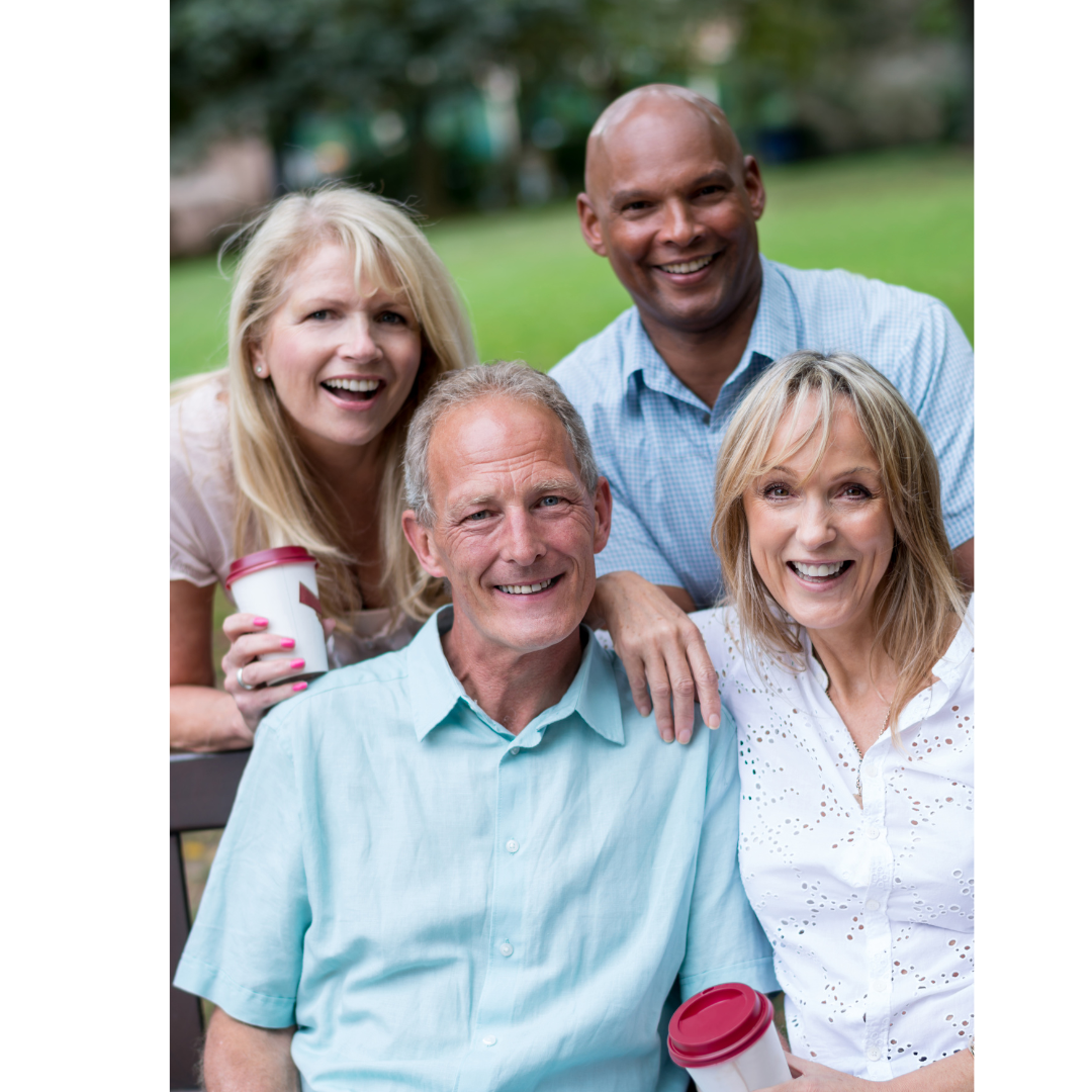 a group of four adults of diverse races sitting on a bench in a park