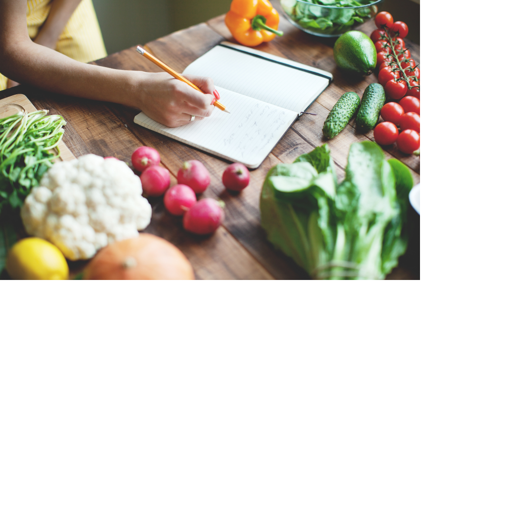 Photo of a person writing in a journal on a table that also has colorful ingredients on it