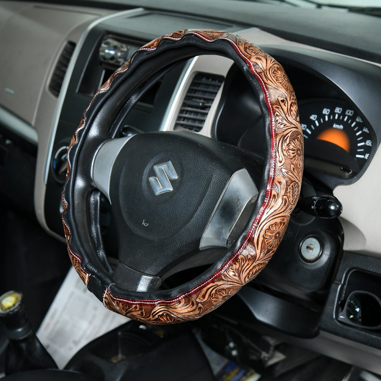 Brown embossed floral leather steering wheel cover on a black Suzuki car interior.