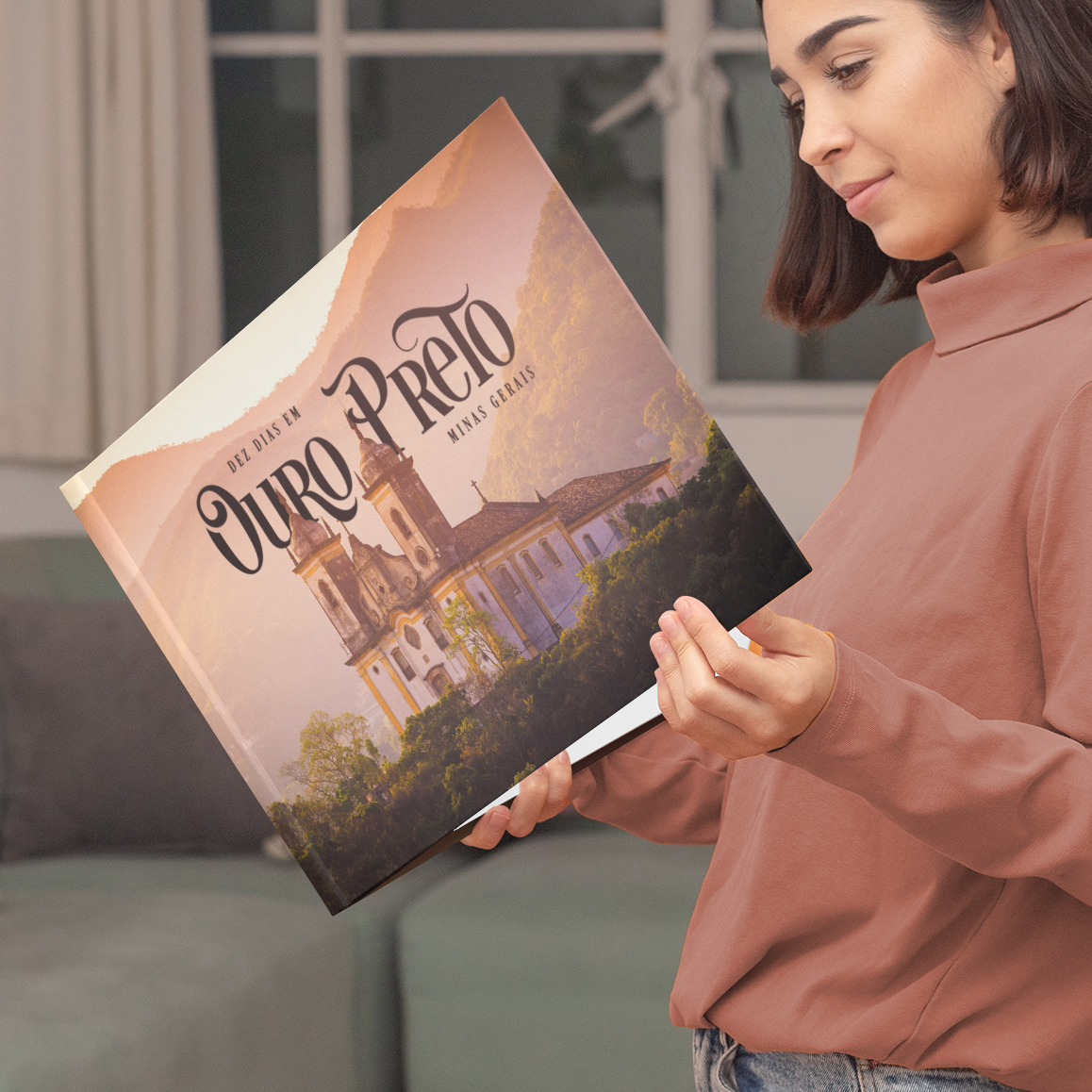 Mulher sorrindo ao folhear álbum de viagem personalizado de Ouro Preto na sala de estar.