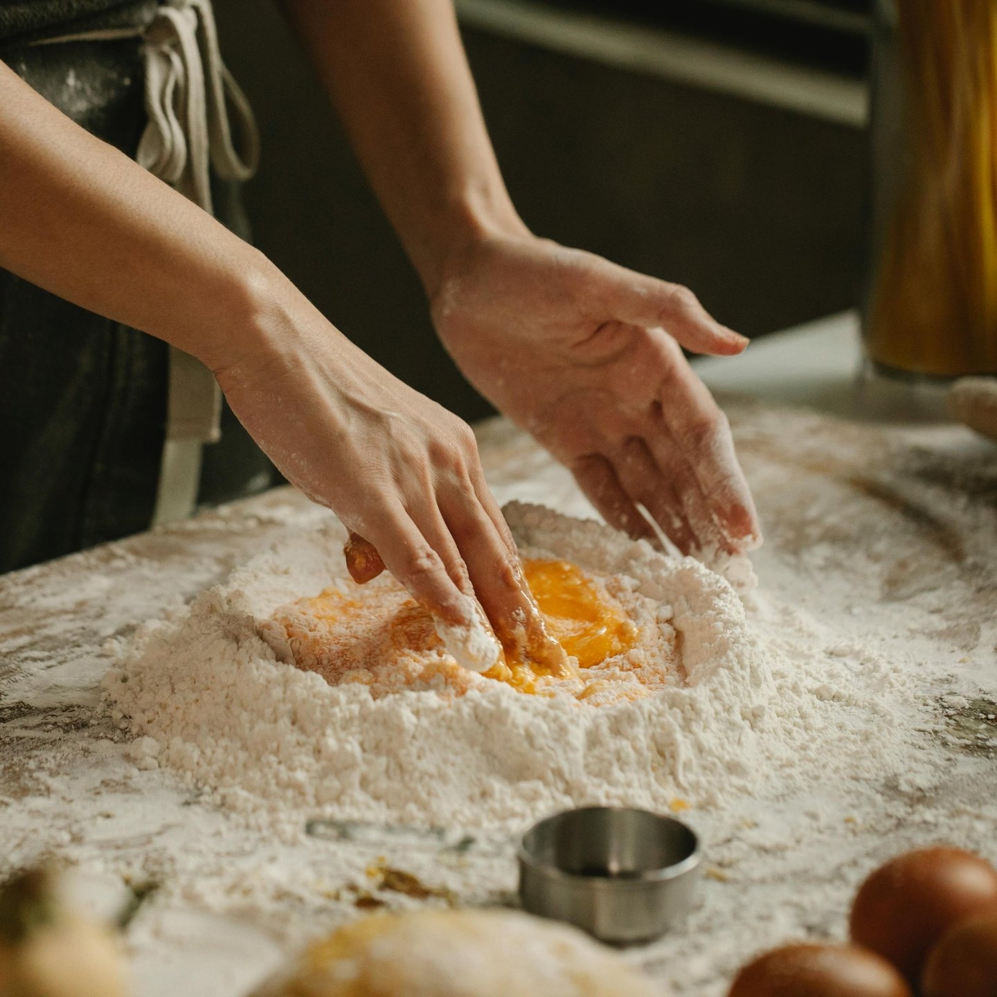 A chef's hands mixing fresh egg yolks into a mound of flour to make homemade pasta dough.
