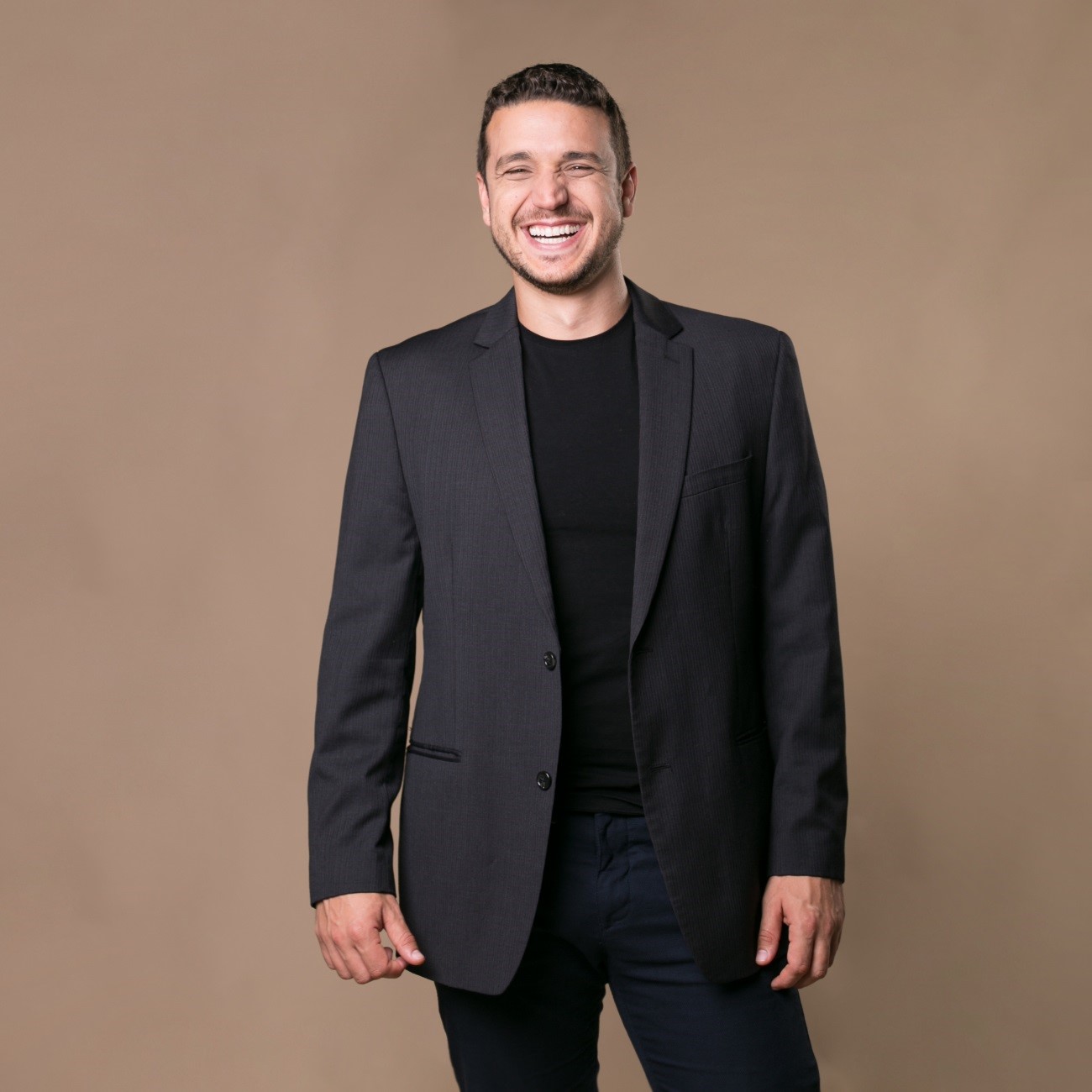 Smiling professional man in a black blazer and t-shirt posing for a corporate headshot.