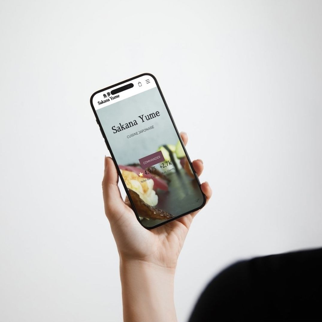 Main tenant un smartphone affichant l'interface du site web de Sakana Yume, que j'ai crée