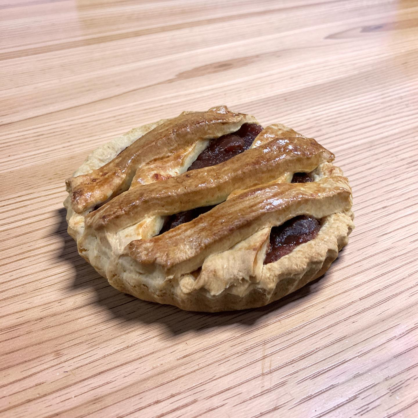 Mini pastel de manzana marrón dorado con una corteza de celosía sobre una mesa de madera ligera.