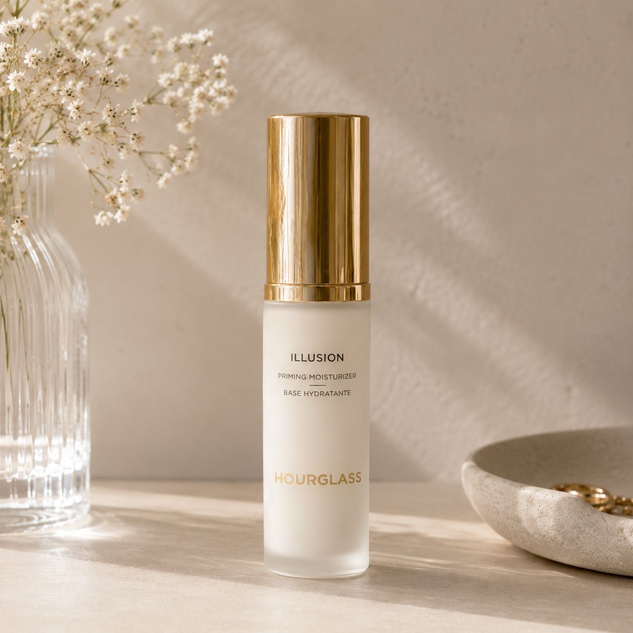 Hourglass Illusion Priming Moisturizer surrounded by luxury makeup products in a soft beige.