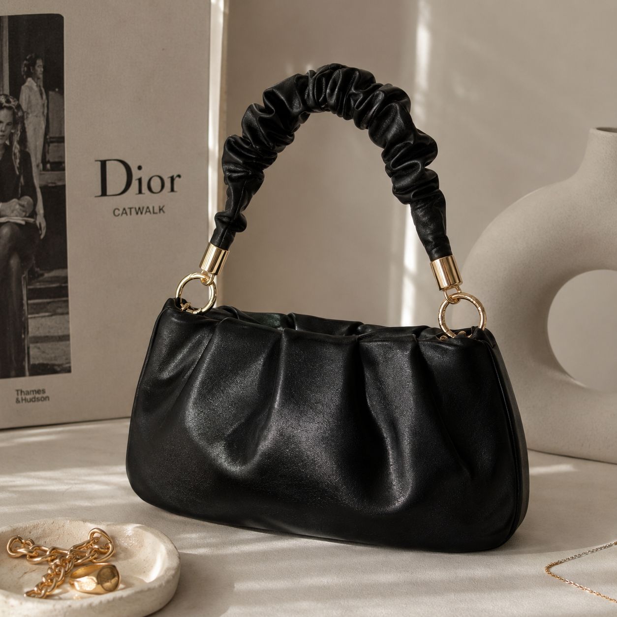 Black ruched shoulder bag with gold hardware styled in a beige luxury aesthetic.