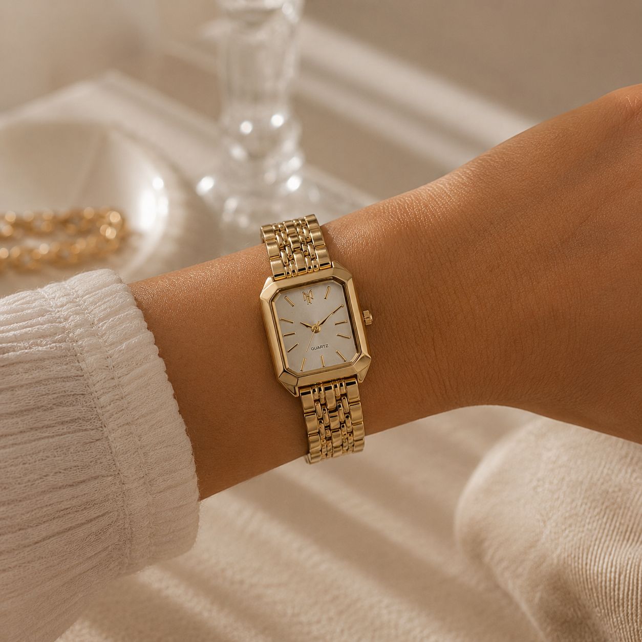 Close-up of a gold luxury watch worn on a woman’s wrist in a soft beige aesthetic setting