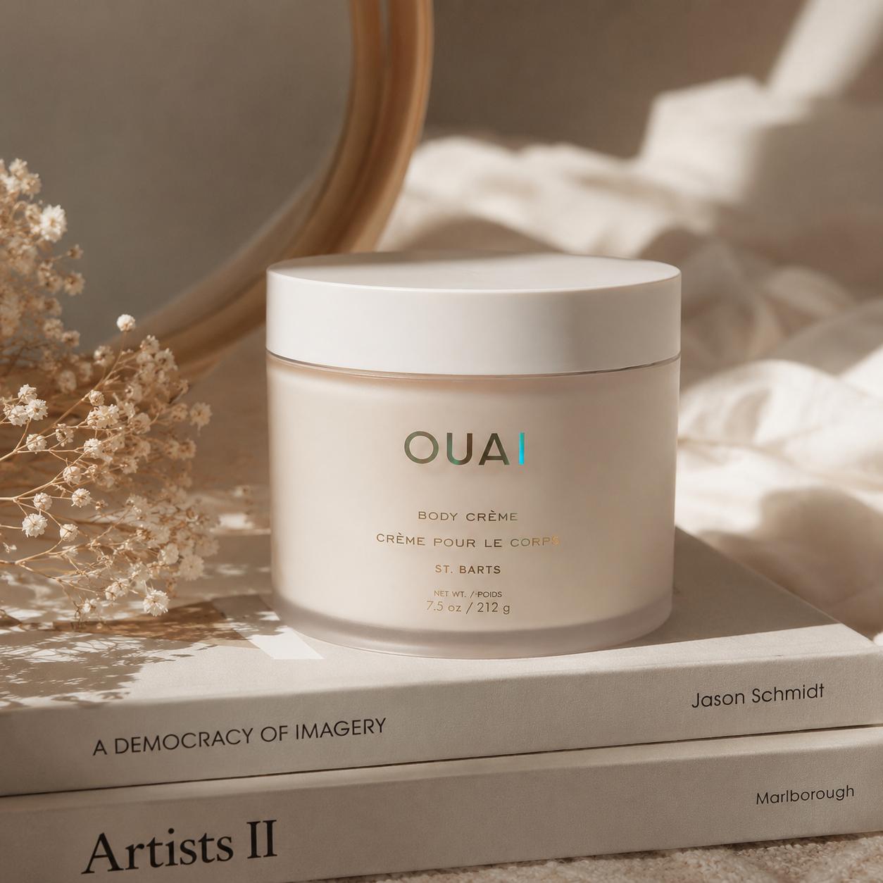 Aesthetic close-up of OUAI Body Crème placed on neutral books with soft beige lighting