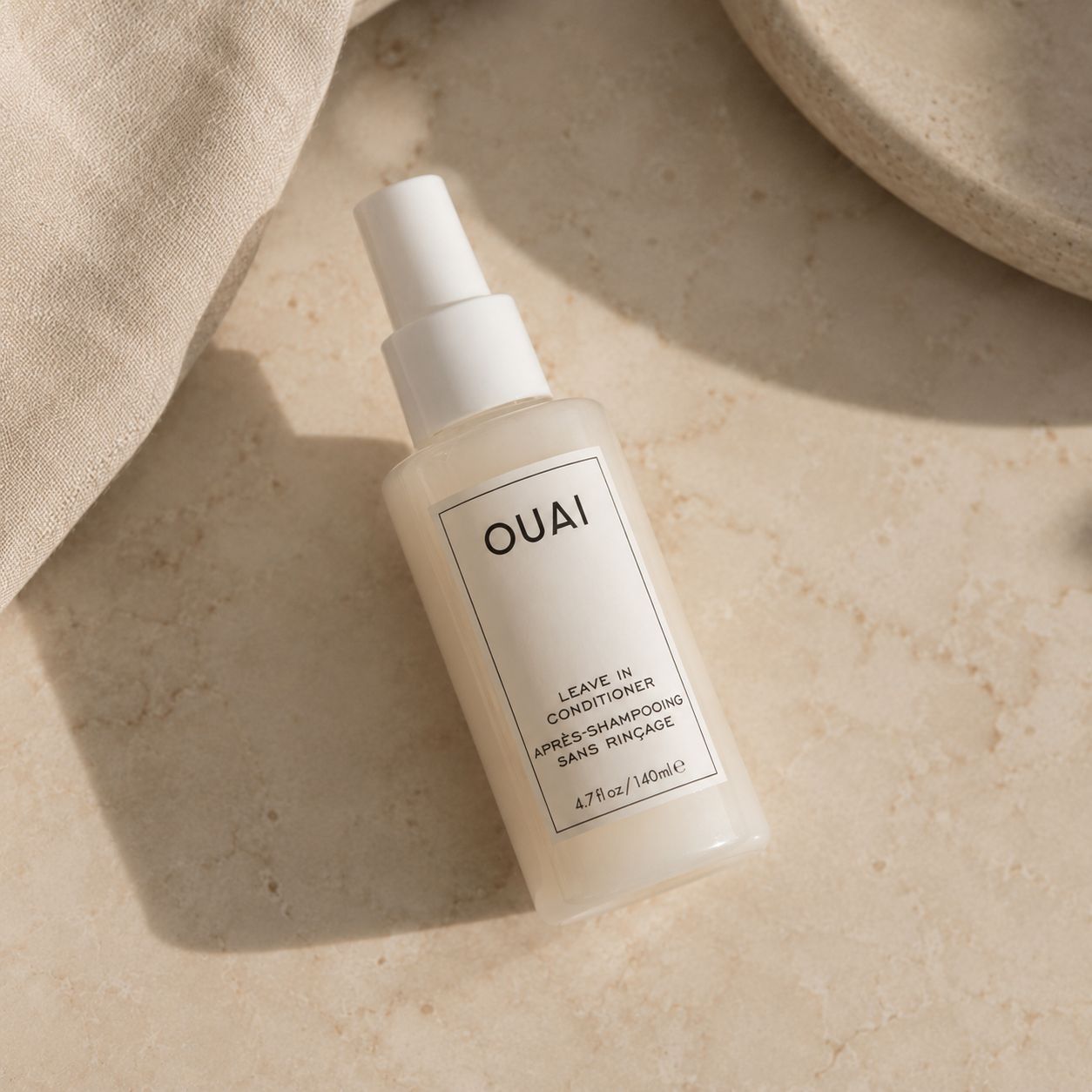 OUAI Leave In Conditioner bottle styled on a beige marble surface.