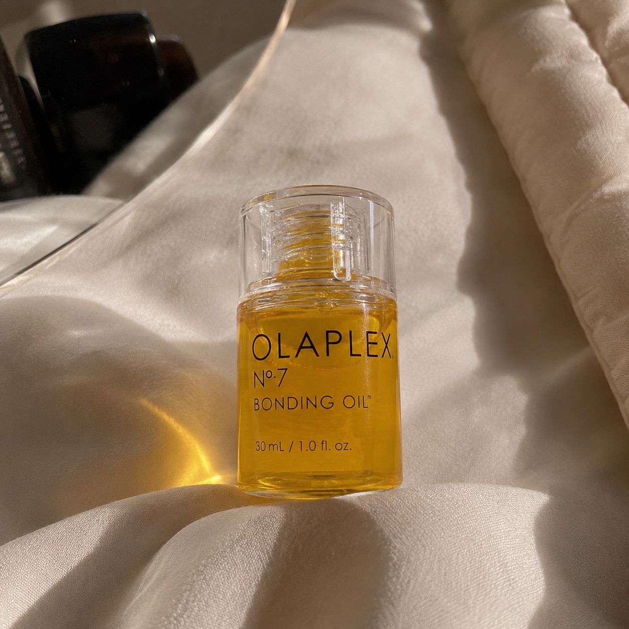Close-up aesthetic photo of Olaplex No.7 Bonding Oil on soft beige satin fabric.