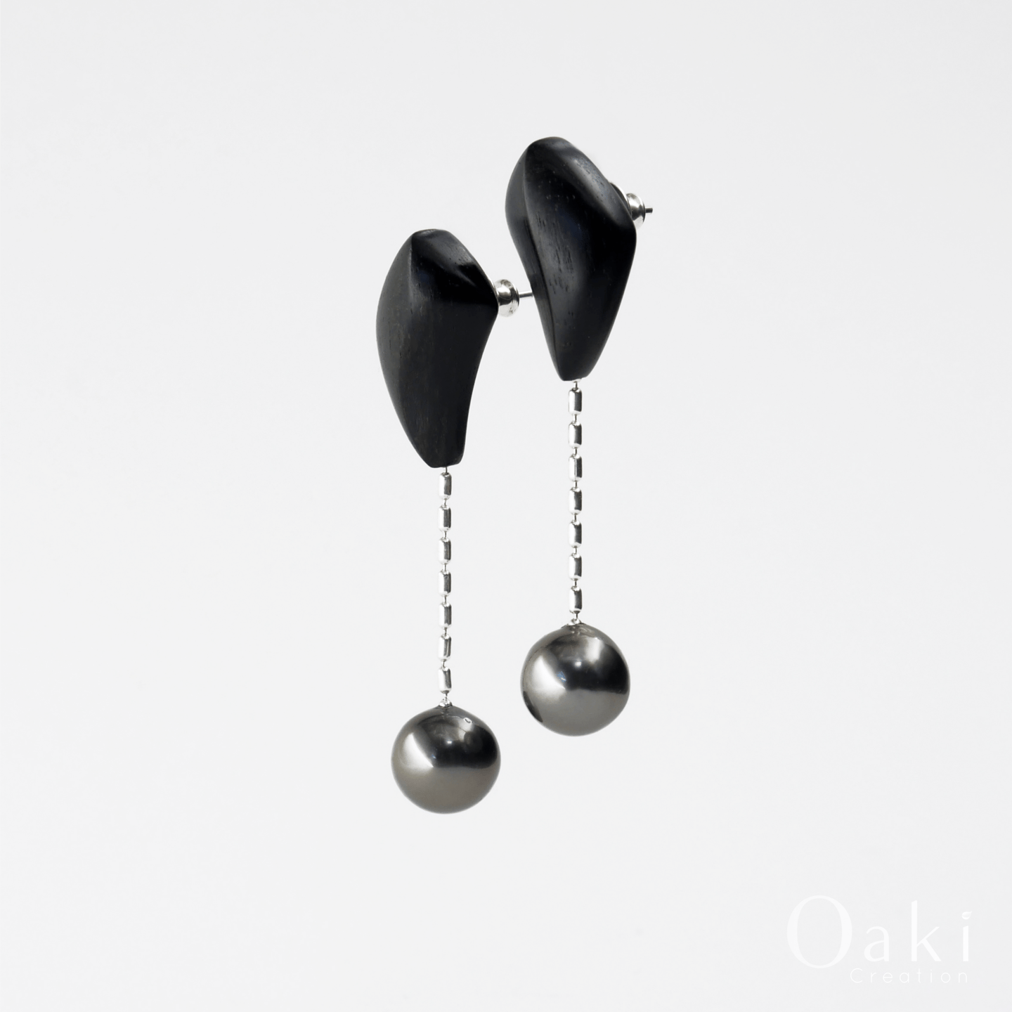 Handcrafted black wood drop earrings featuring silver chains and grey Tahitian pearls.
