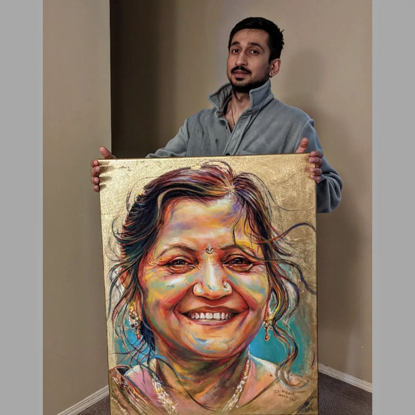 Artist S.K. Gusani holding a memorial painting of a smiling woman, gold leaf, portrait art