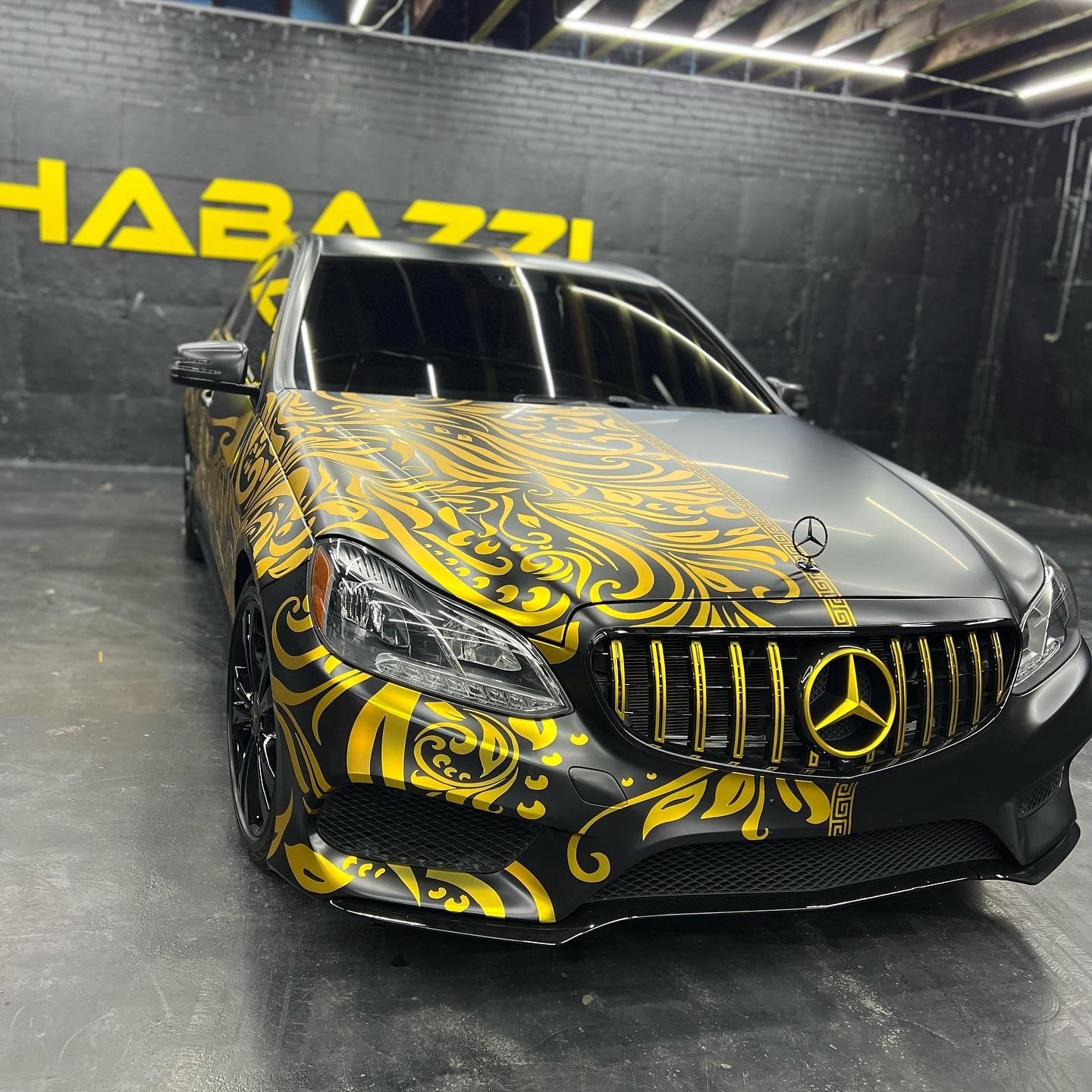 Custom matte black Mercedes-Benz with a gold baroque patterned vinyl wrap and a matching gold grille.