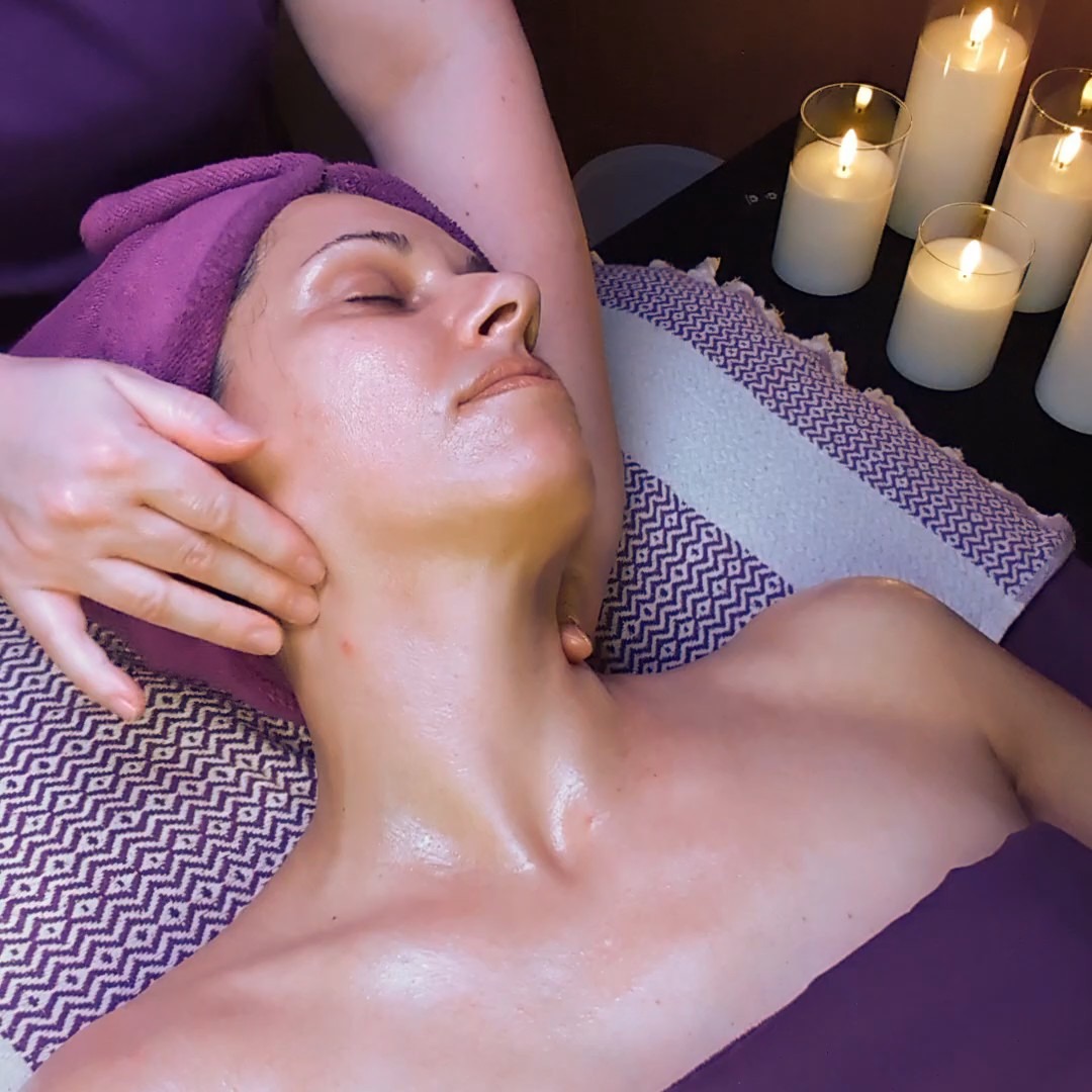 A woman receives a relaxing facial massage at a luxury spa with lit candles nearby.