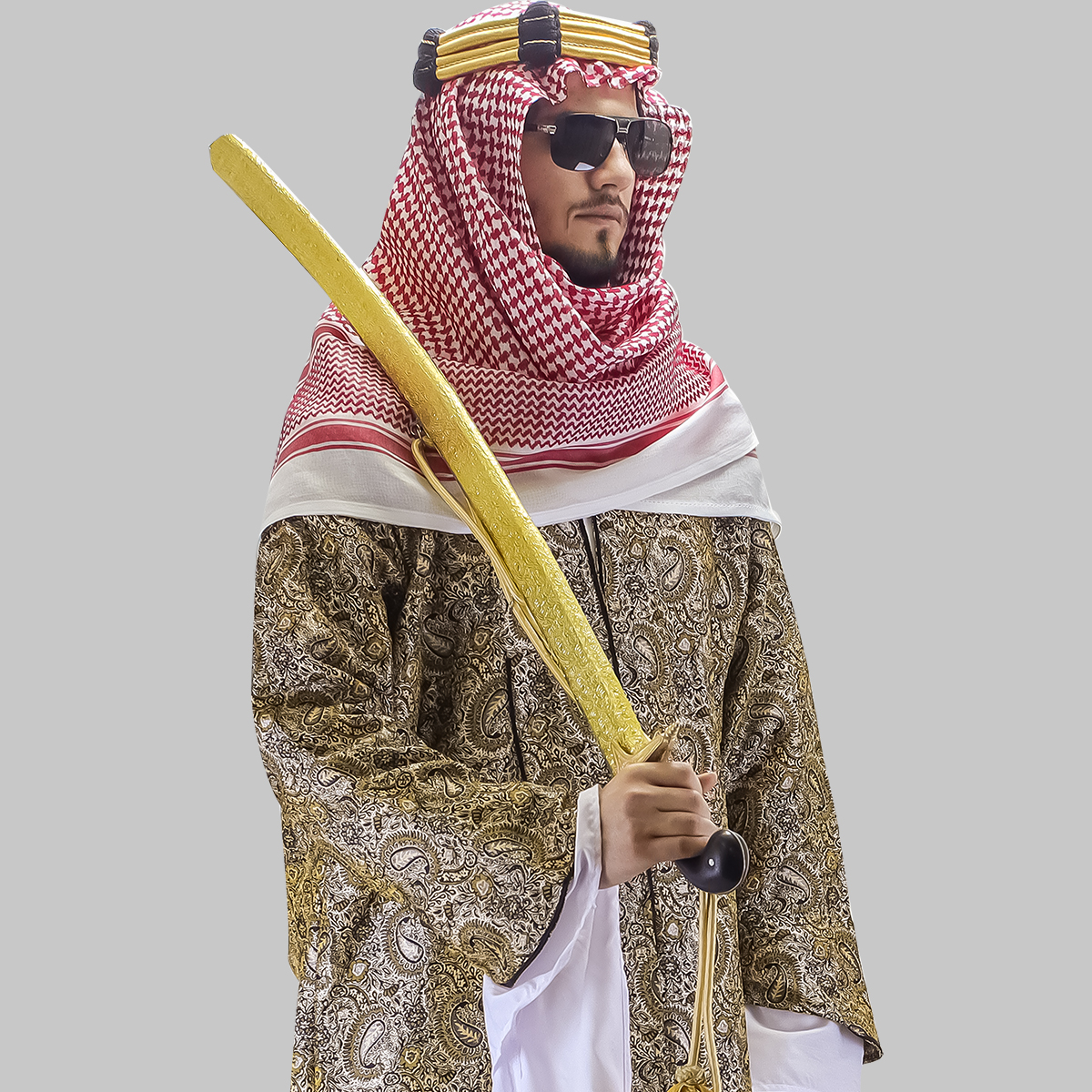 Saudi man in traditional thobe, bisht, and shemagh holding a golden prop sword.